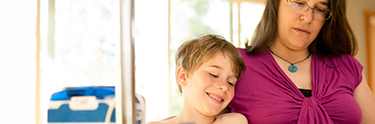 Small, shirtless boy and mom sitting in office with tube-feeding equipment