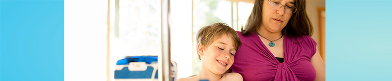 Small, shirtless boy and mom sitting in office with tube-feeding equipment